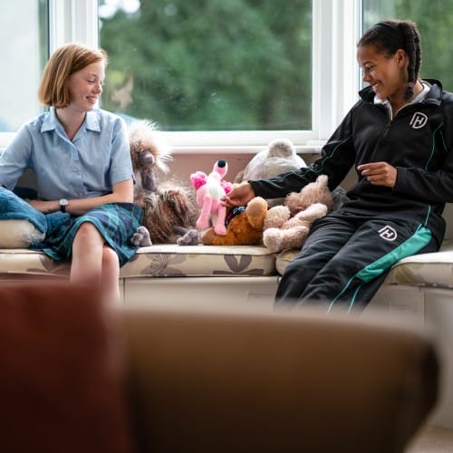Two 12 year olds sat on a bench with teddies in boarding house