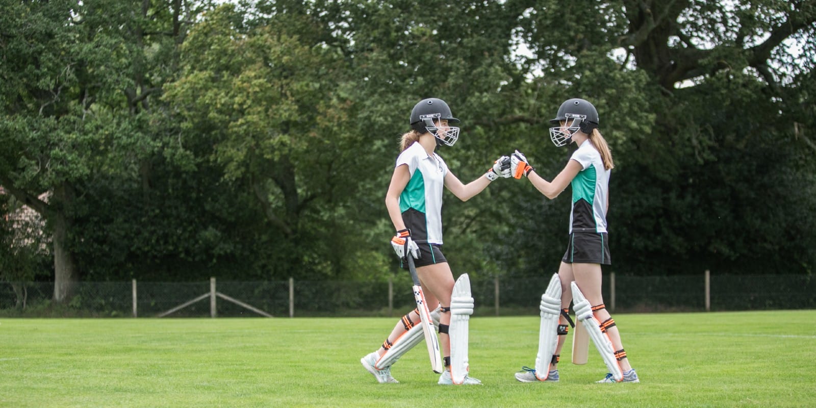 Two girls in cricket kit fist bump