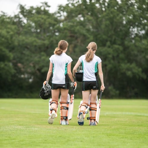 Two girls in cricket kit walk on to pitch